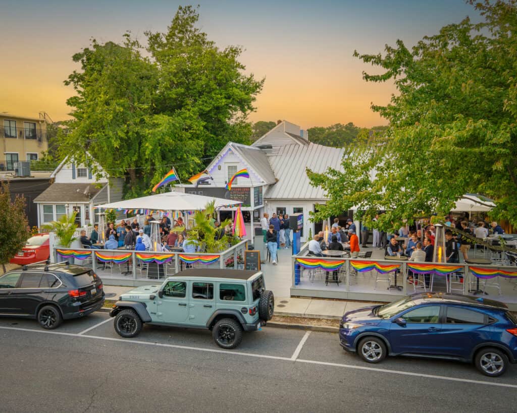 Scenic view of a gay bar adorned with rainbow bunting as the sun sets in Rehoboth Beach, a vibrant LGBTQ+ friendly destination for nightlife and community.