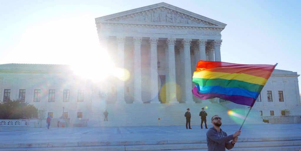 A gay man proudly waving a rainbow flag in front of the United States Supreme Court in Washington DC, advocating for LGBTQ+ rights and equality. The iconic landmark serves as a backdrop for the expression of inclusivity and activism in the nation's capital.
