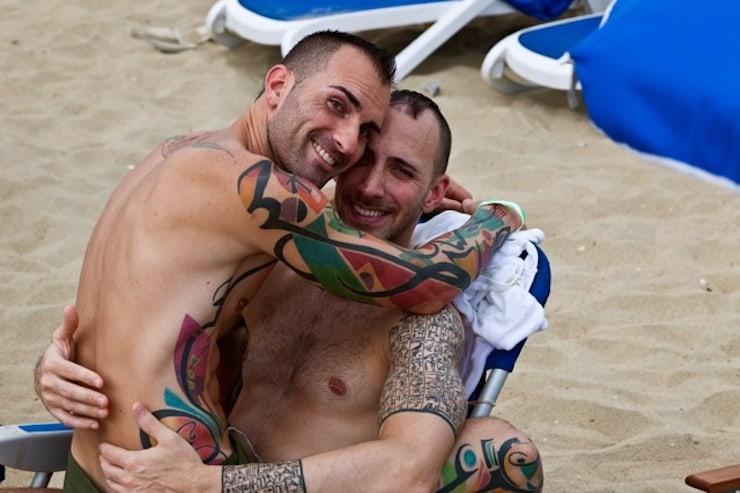 Attractive gay couple with tattoos enjoying each other's company on Asbury Park beach, reflecting the city's inclusive atmosphere and beach lifestyle.