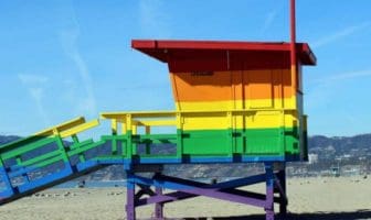 View of a wooden hut painted in rainbow colors standing on a beach.