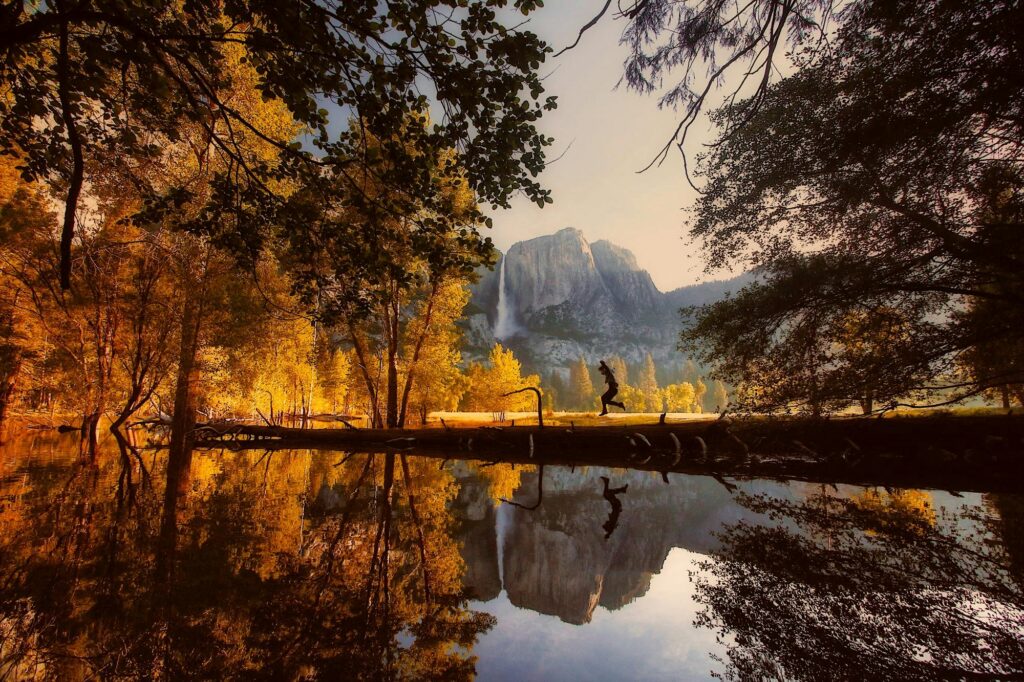 Hiker enjoying golden autumn trees and mountain reflections in Yosemite Valley during a California fall foliage road trip.
