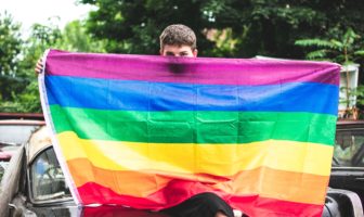 Gay man joyfully waving rainbow flag at Spring LGBTQ+ pride event, celebrating diversity and inclusion.