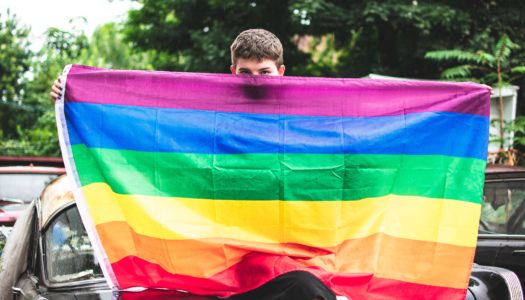 Gay man joyfully waving rainbow flag at Spring LGBTQ+ pride event, celebrating diversity and inclusion.