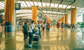 Travelers walking through a bright, busy airport terminal with luggage and check-in counters, representing the crowds highlighted in Thanksgiving travel advice tips.