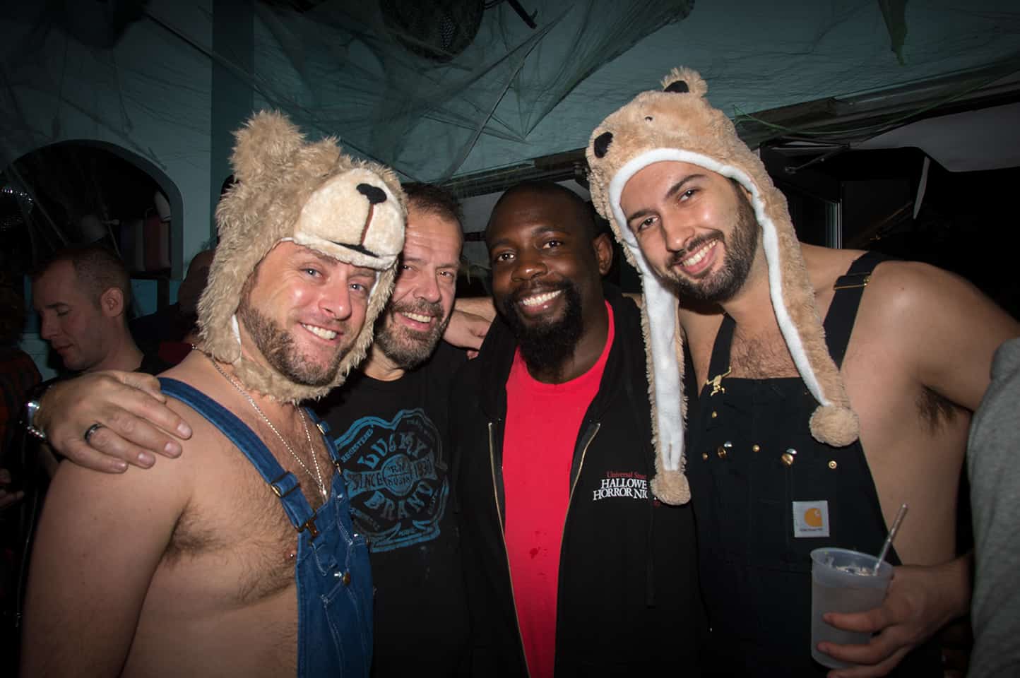 Four friends having a blast at Spooky Bear in Provincetown, a popular LGBTQ+ halloween event, wearing bear hats and trendy overalls.