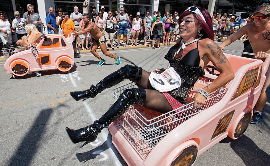 Men in drag being pushed in shopping carts designed as race cars during Key West's Conch Republic Drag Race, part of the Conch Republic Independence Celebration in April, a vibrant LGBTQ+ event.