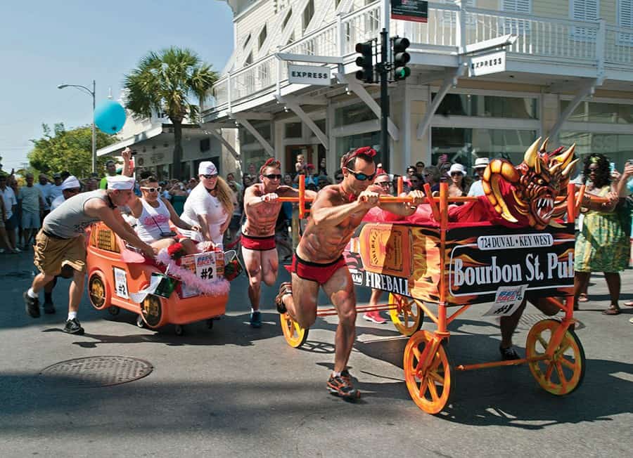Men in drag being pushed in shopping carts designed as race cars during Key West's Conch Republic Drag Race, part of the Conch Republic Independence Celebration in April, a vibrant LGBTQ+ event.