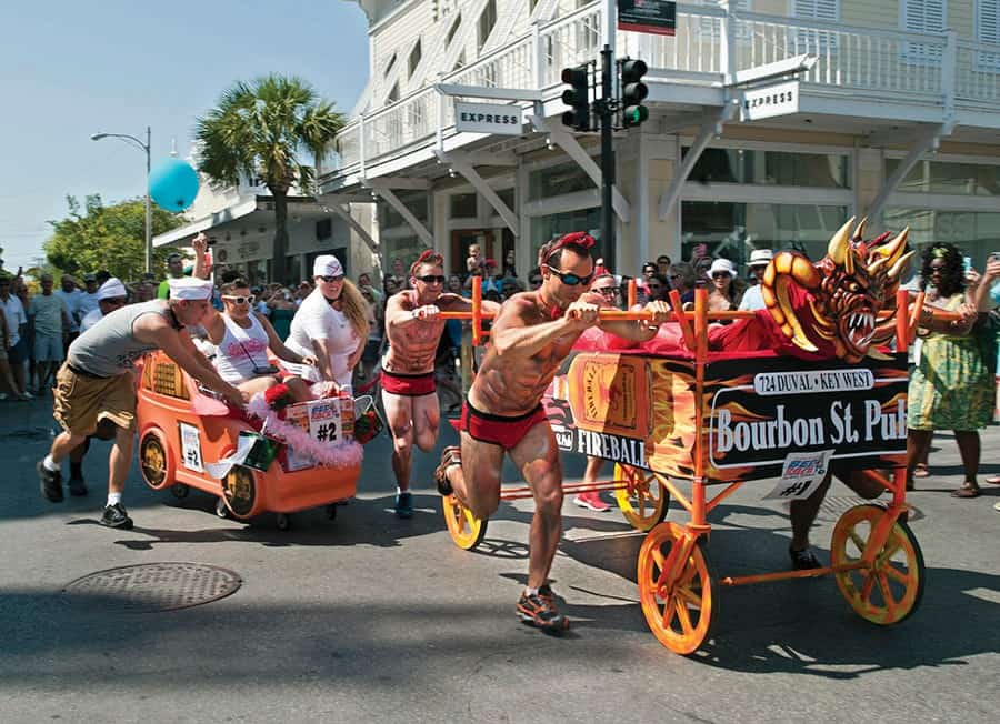 Men in drag being pushed in shopping carts designed as race cars during Key West's Conch Republic Drag Race, part of the Conch Republic Independence Celebration in April, a vibrant LGBTQ+ event.