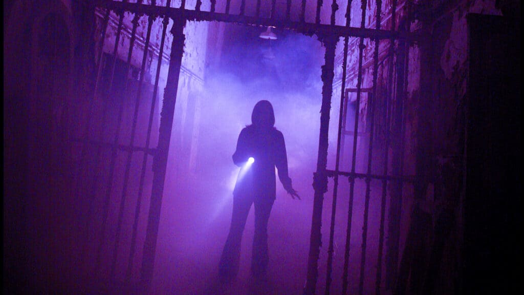 A person stands in a dimly lit room at Eastern State Penitentiary, illuminated by a haunting purple light at one of the top haunted houses in the USA.