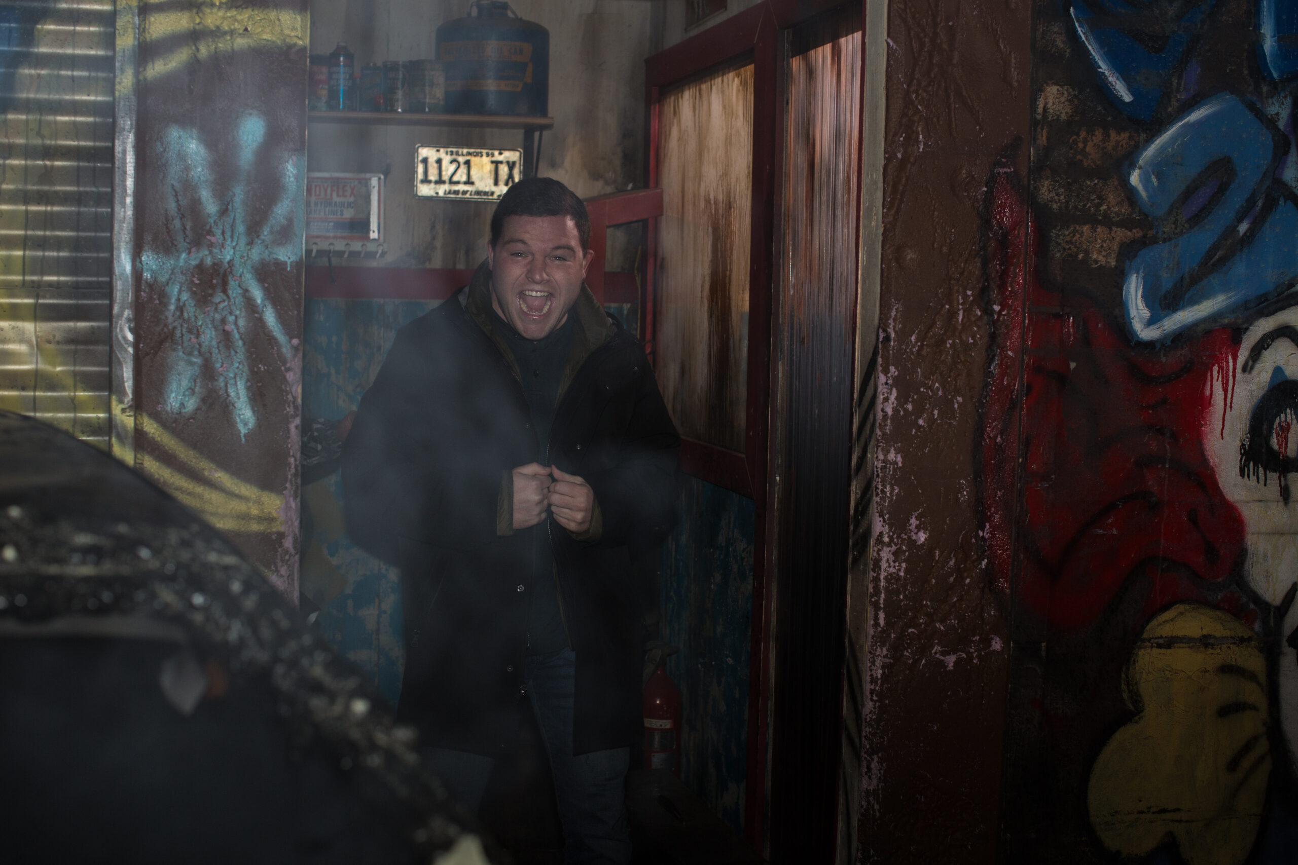 A man confidently poses in front of a door adorned with vibrant graffiti artwork at Chicago's 13th Floor Haunted House, one of the top haunted houses in the USA.