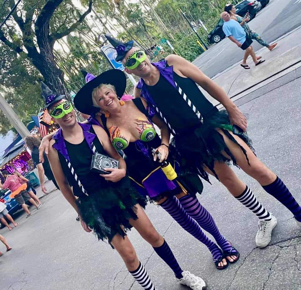 Two men and one women wearing witch costumes, complete with pointed hats and tutu's pose for a Halloween-themed photograph at Fantasy Fest.