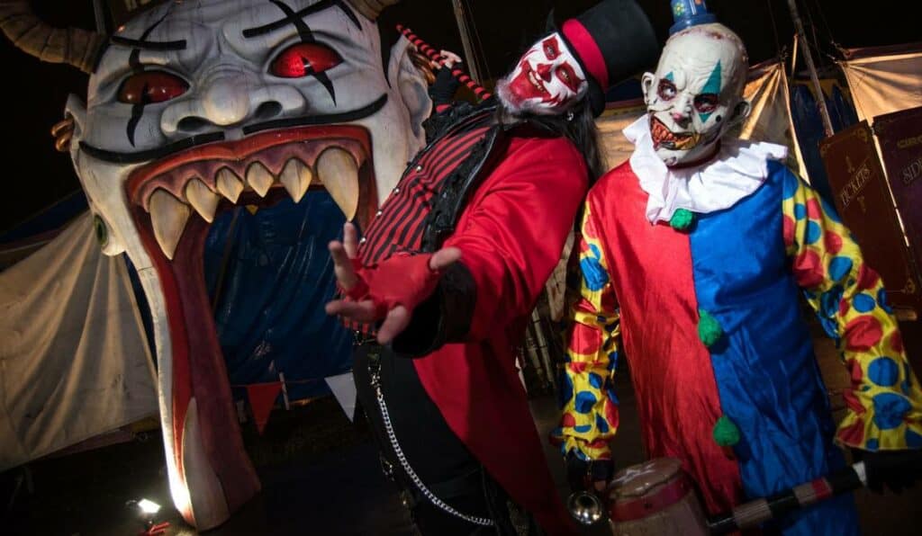 A pair of clowns, adorned in traditional clown garb, stand beside a massive clown head, exuding a sense of horror at Miami's House of Horror Haunted Carnival, one of the top haunted houses in the USA.