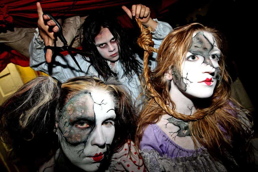 Three women adorned with artistic face paint and makeup, showcasing their unique and captivating expressions at Fort Worth's Cutting Edge, a top haunted house in the USA.