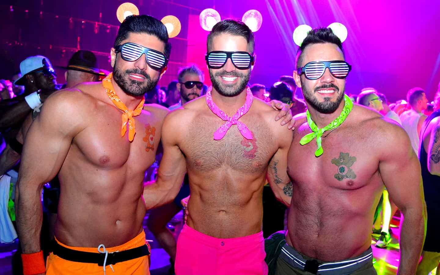 Three shirtless men dancing at a vibrant circuit party during the Miami Winter Party Festival, a celebration of LGBTQ+ culture and unity.