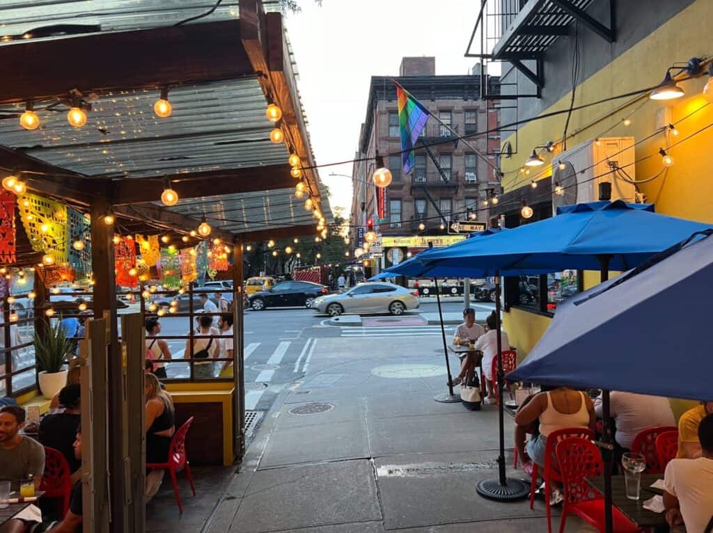 A lively outdoor restaurant scene at Arriba Arriba in New York City, featuring string lights, colorful decorations, and umbrellas, as people dine and celebrate in a vibrant atmosphere.