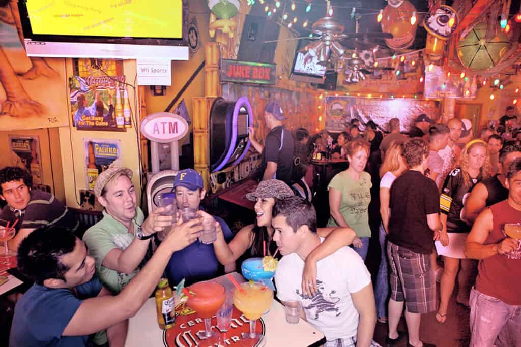 A lively Cinco de Mayo bar scene at Fiesta Cantina, with people clinking glasses, colorful drinks, and festive decorations filling the space with energy and celebration.