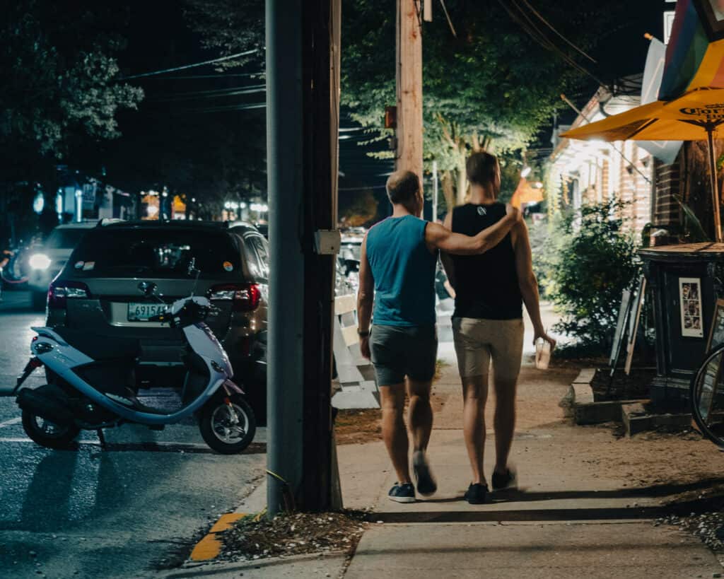 Two men strolling down the vibrant streets of Rehoboth Beach, one with his arm affectionately draped over the other, enjoying a LGBTQ+-friendly getaway.