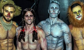 Four gay shirtless men, adorned in body-painted Wizard of Oz costumes, pose in a playful group photograph.