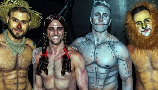 Four gay shirtless men, adorned in body-painted Wizard of Oz costumes, pose in a playful group photograph.