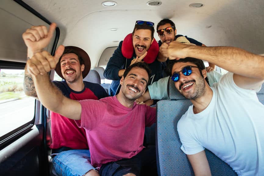 Group of young, excited hipster men inside a van during a spring road trip. LGBTQ+ travelers enjoy adventure and camaraderie on the open road.