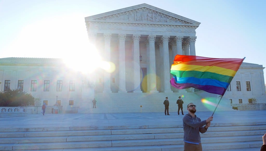 Gay man proudly waving Pride flag in front of Supreme Court, symbolizing LGBTQ+ rights and activism.