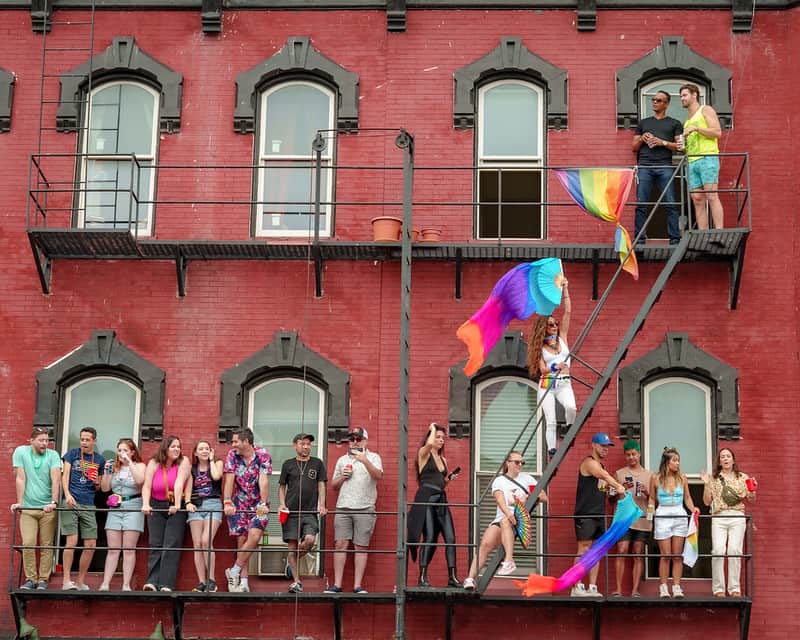 LGBTQ+ group on NYC fire escape watching pride parade, celebrating diversity and inclusion.