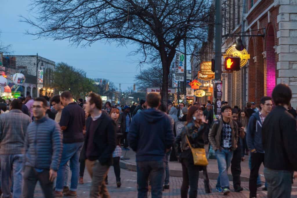 Group of people enjoying the vibrant atmosphere of South by Southwest (SXSW) on a bustling street in Austin, Texas, surrounded by a variety of restaurants and eateries.