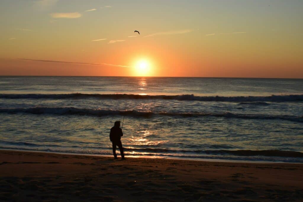 Gay man fishing on Asbury Park beach at sunrise, embracing the serene beauty and inclusive atmosphere of the coastal community.