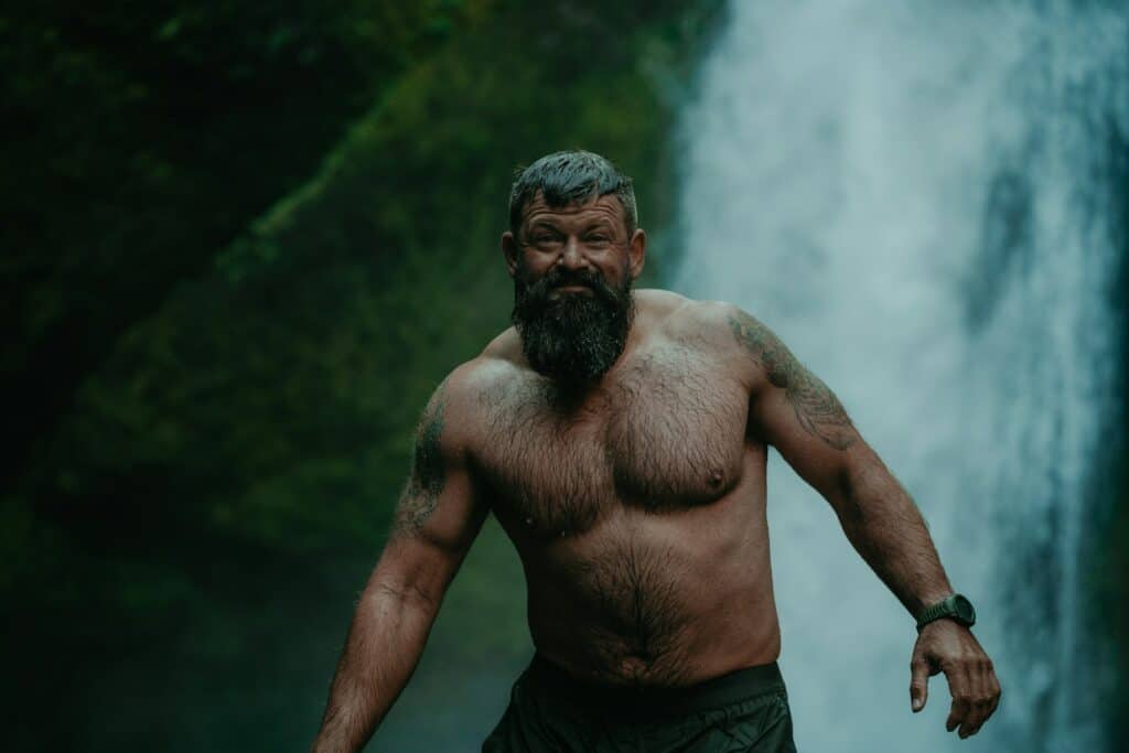 Tattooed bearded man enjoying waterfall, embracing nature's beauty and serenity.