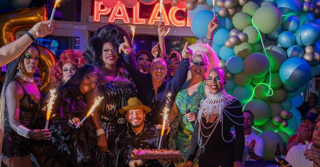 Colorful drag queens strike a pose outside Palace Bar & Restaurant in South Beach, exuding glamour and confidence against a lively backdrop.