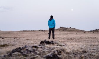 Gay man in blue hoodie standing confidently on brown grass, representing LGBTQ+ empowerment and individuality.