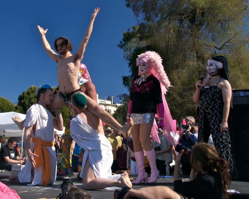 A Jesus lookalike is held up by two men as nuns from The Sisters of Perpetual Indulgence look on at the Hunky Jesus and Foxy Mary contest in San Francisco, celebrating diversity and inclusivity in the LGBTQ+ community.