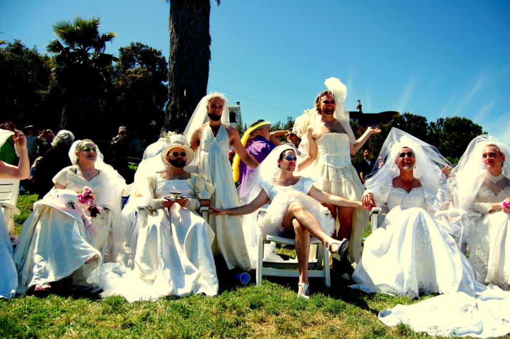 A group of onlookers dressed as brides observe the Hunky Jesus and Foxy Mary contest in San Francisco, adding to the colorful celebration of diversity and inclusivity in the LGBTQ+ community.