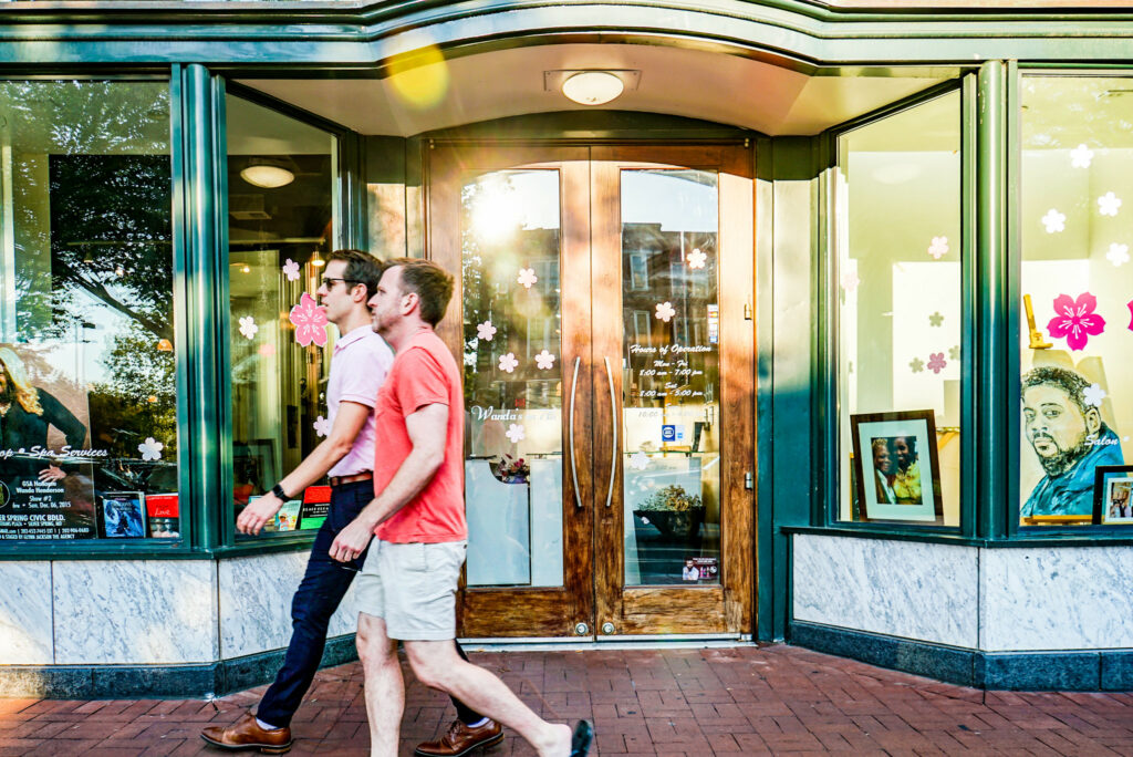 Two gay men strolling through the vibrant streets of a neighborhood in Washington DC. The area is known for its inclusive atmosphere, LGBTQ+ friendly establishments, and colorful community events, contributing to the rich tapestry of diversity in the nation's capital.