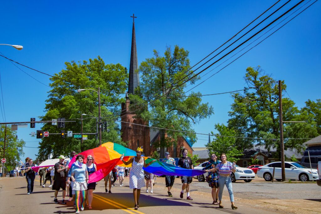 Group carrying a rainbow flag at Oxford, MS Pride parade, with joyful spectators celebrating diversity in spring LGBTQ+ pride events.