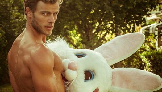 Shirtless man holding plush bunny rabbit head, a playful image representing LGBTQ+ Easter celebrations and gay-friendly getaways.