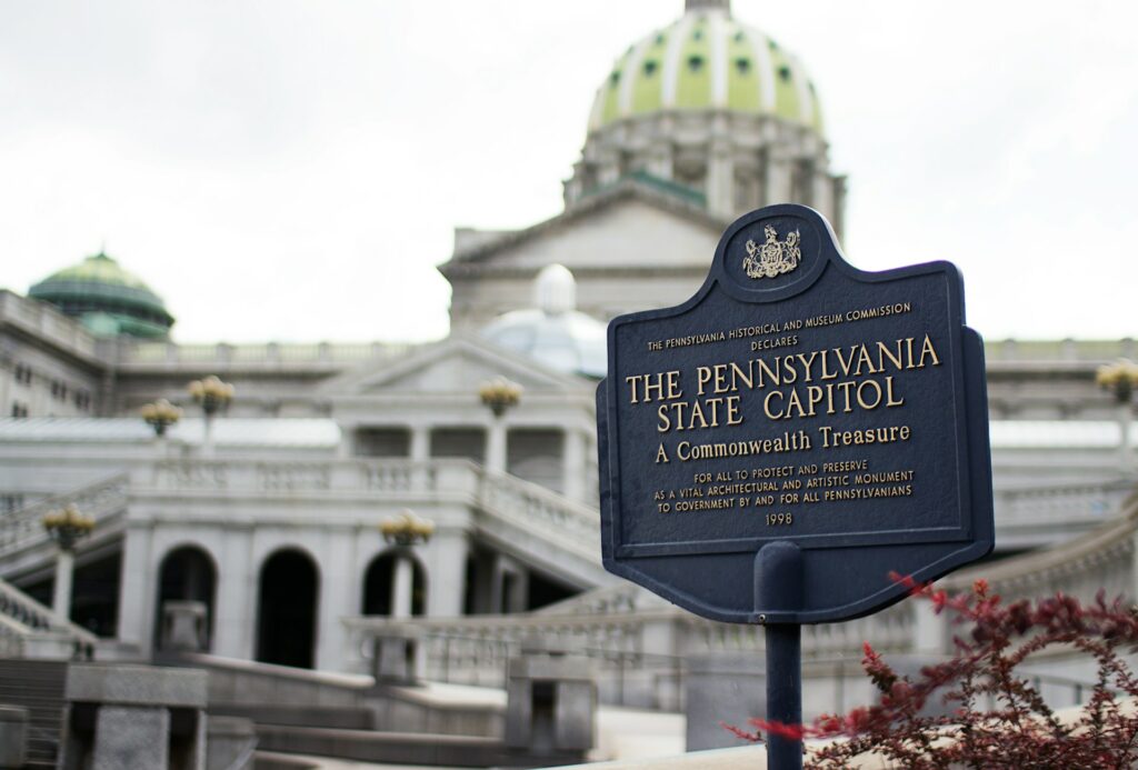 Pennsylvania State Capitol signage with the capitol building in the background. Explore historic landmarks on your Keystone state road trip.