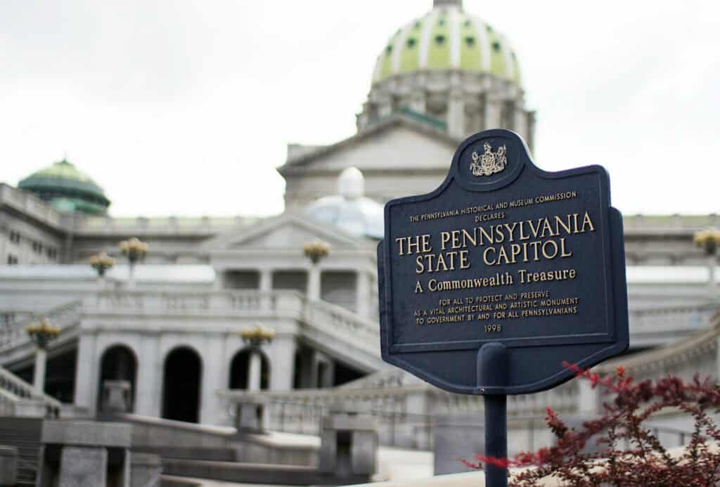 Pennsylvania State Capitol signage with the capitol building in the background. Explore historic landmarks on your Keystone state road trip.