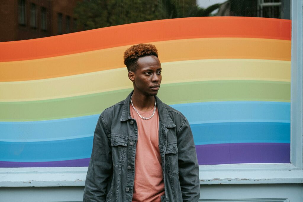Contemplative black man stands against window painted in LGBT colors, symbolizing reflection and inclusivity in LGBTQ travel.