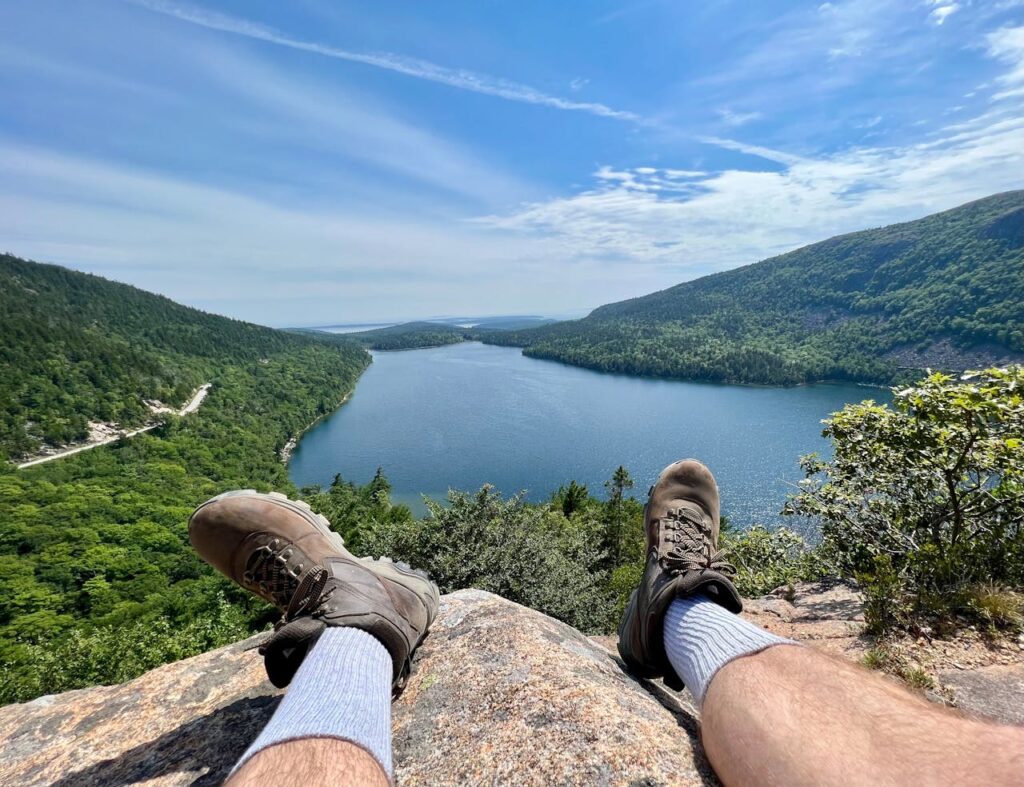 Gay man sitting on a rock, overlooking Jordan Pond in Acadia National Park. LGBTQ+ travelers enjoy scenic beauty on spring road trips.