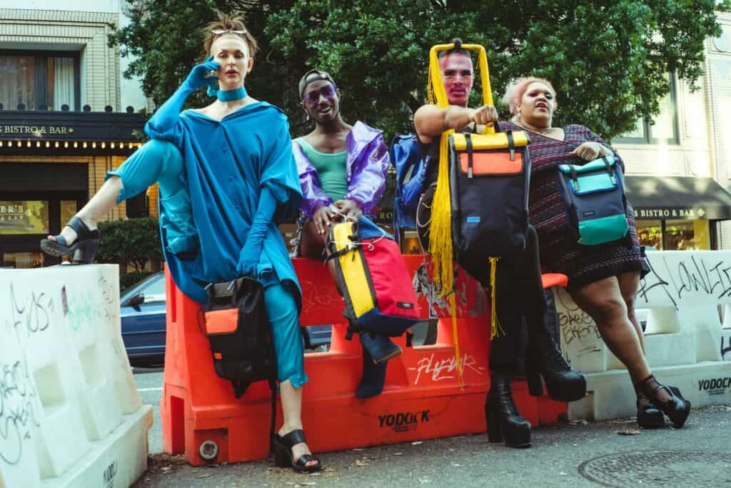 Group of LGBTQ+ travelers leaning against road barrier, symbolizing solidarity and safety in travel.