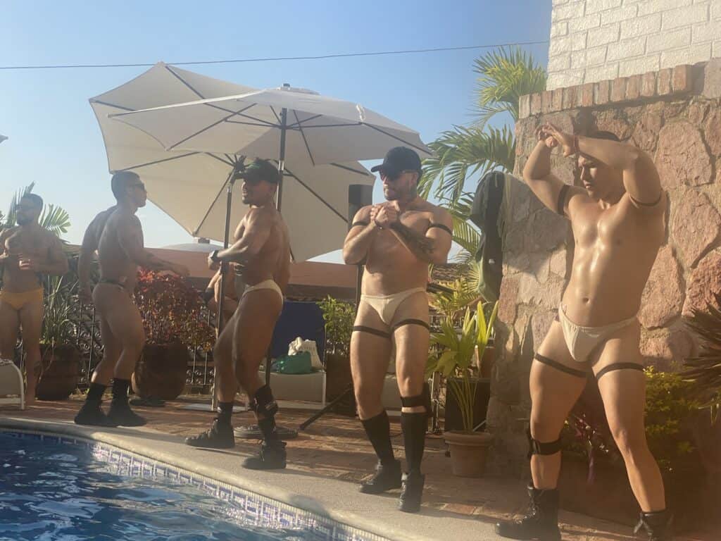 Five shirtless men in swimwear dance by a pool in Puerto Vallarta, enjoying the sunny day and embracing the city's inclusive LGBTQ+ atmosphere.