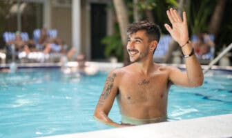 A smiling man in a pool at Island House Key West waving. He has tattoos and short hair.