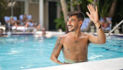 A smiling man in a pool at Island House Key West waving. He has tattoos and short hair.