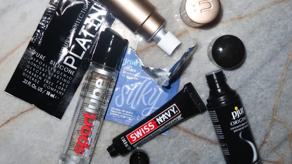 Various personal lubricants on a marble surface, including bottles and sachets — key items among gay travel packing essentials.