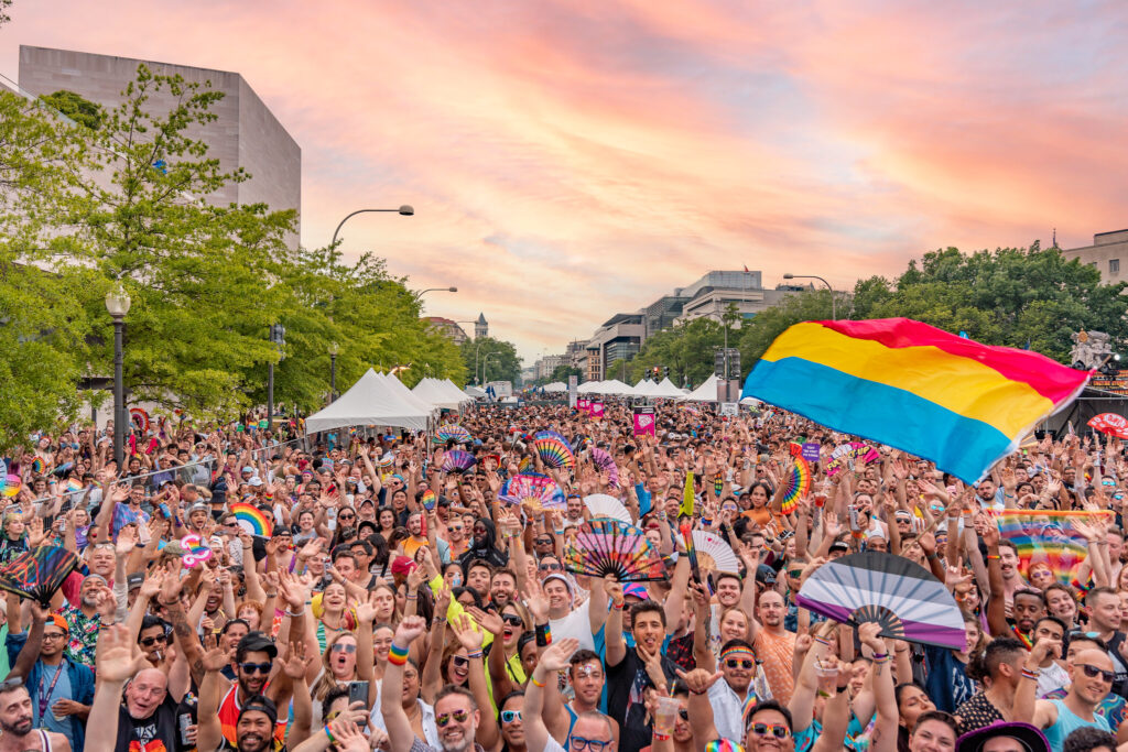 A large crowd celebrating with colorful flags and fans during a Capital Pride event at sunset in Washington, D.C., who is hosting WorldPride 2025.