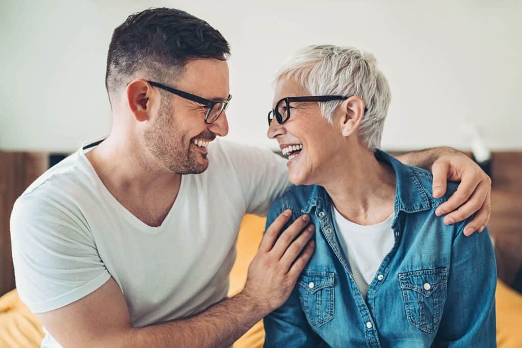 A young gay man and his mother laugh together, sharing a joyful moment while celebrating with thoughtful Mother’s Day travel gifts.