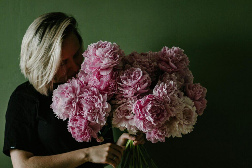 A mother holding a large bouquet of pink peonies against a green wall. 