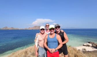 Group of four men smiling near the coast with a blue ocean and green islands in the background, enjoying a naked vacation for men on a trip with Everything To Sea.