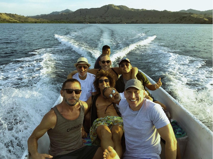 A group of eight friends enjoying a boat ride on a sunny day, smiling and posing together. 